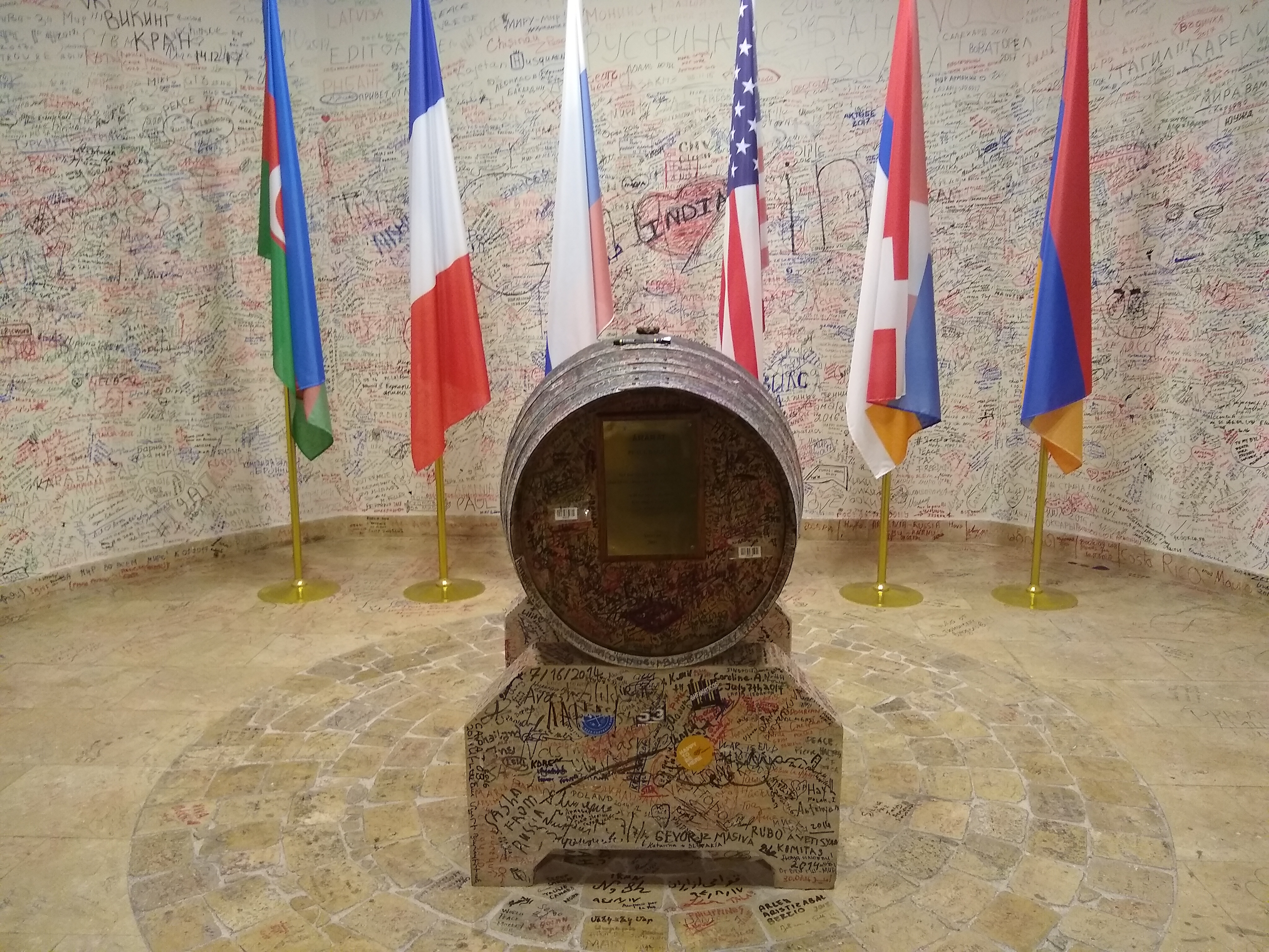 Photo of a barrel, with writing on the barrel and surrounding walls, with the flags of Azerbaijan, France, Russia, the USA, Artsakh and Armenia