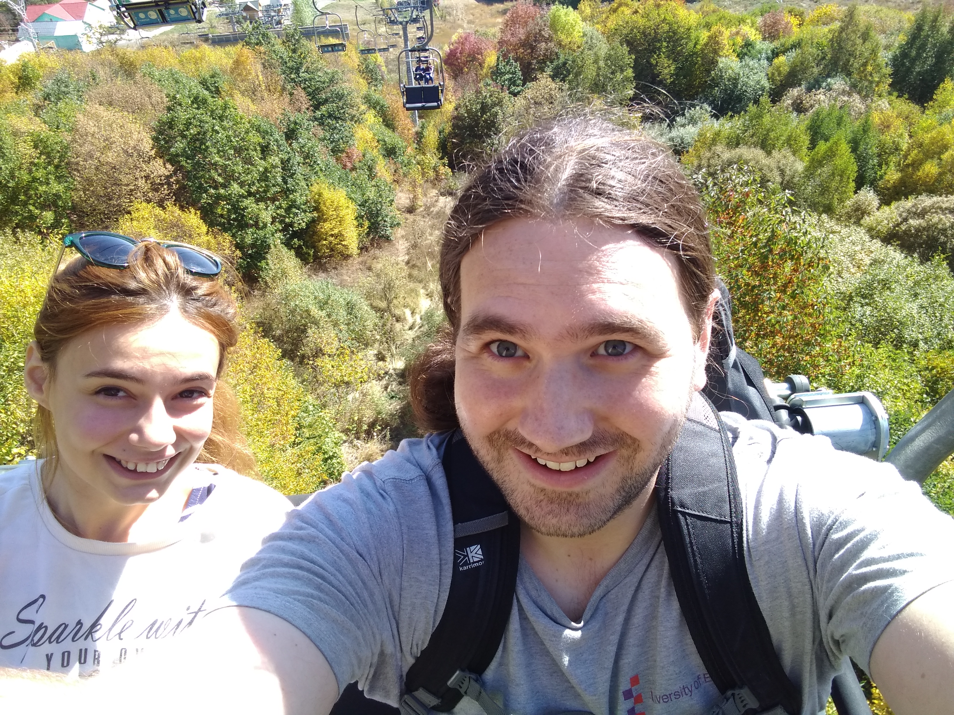 Photo of a man and a woman on a cable car above green trees