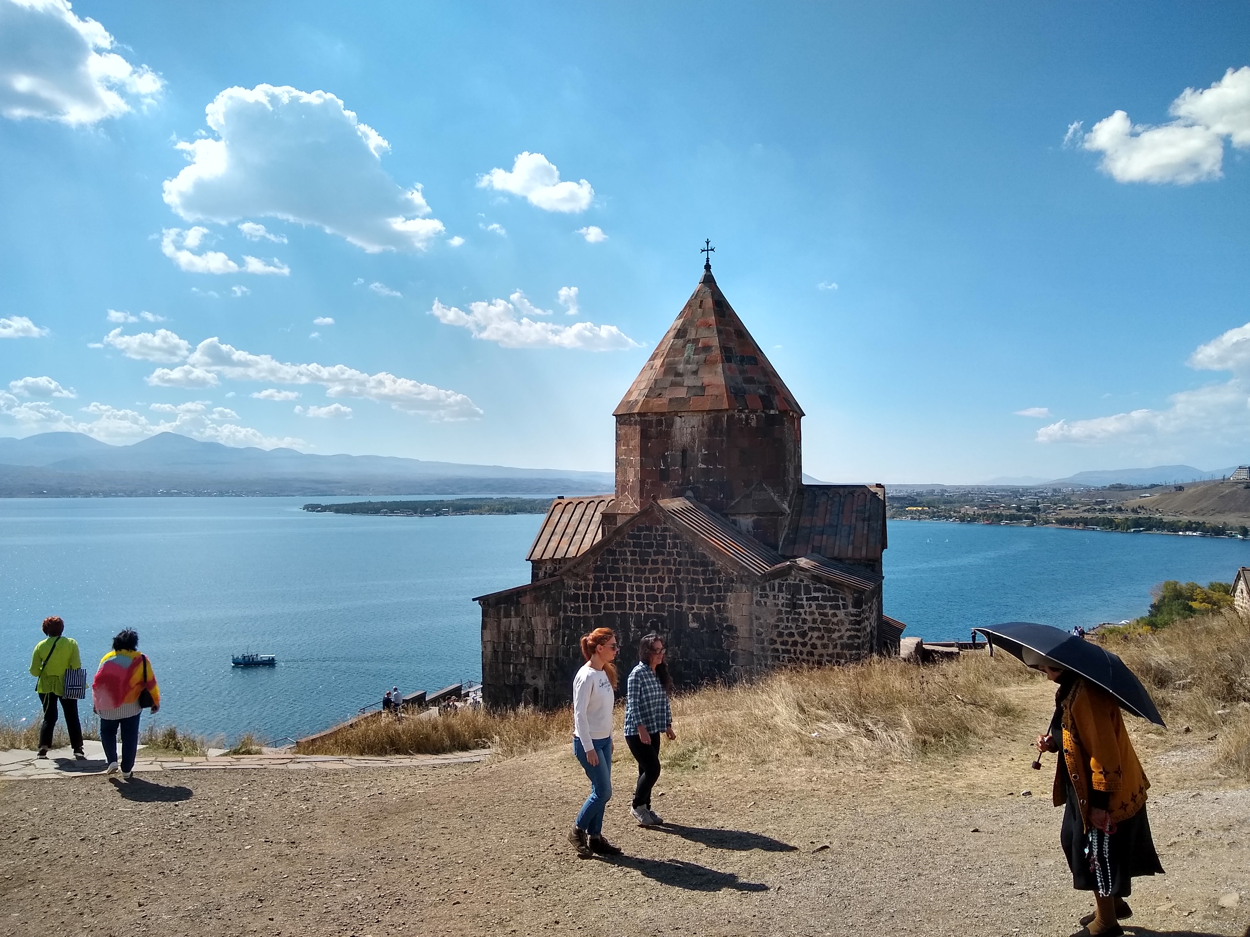 Photo of a small church in the foreground with a lake in the background and people standing around