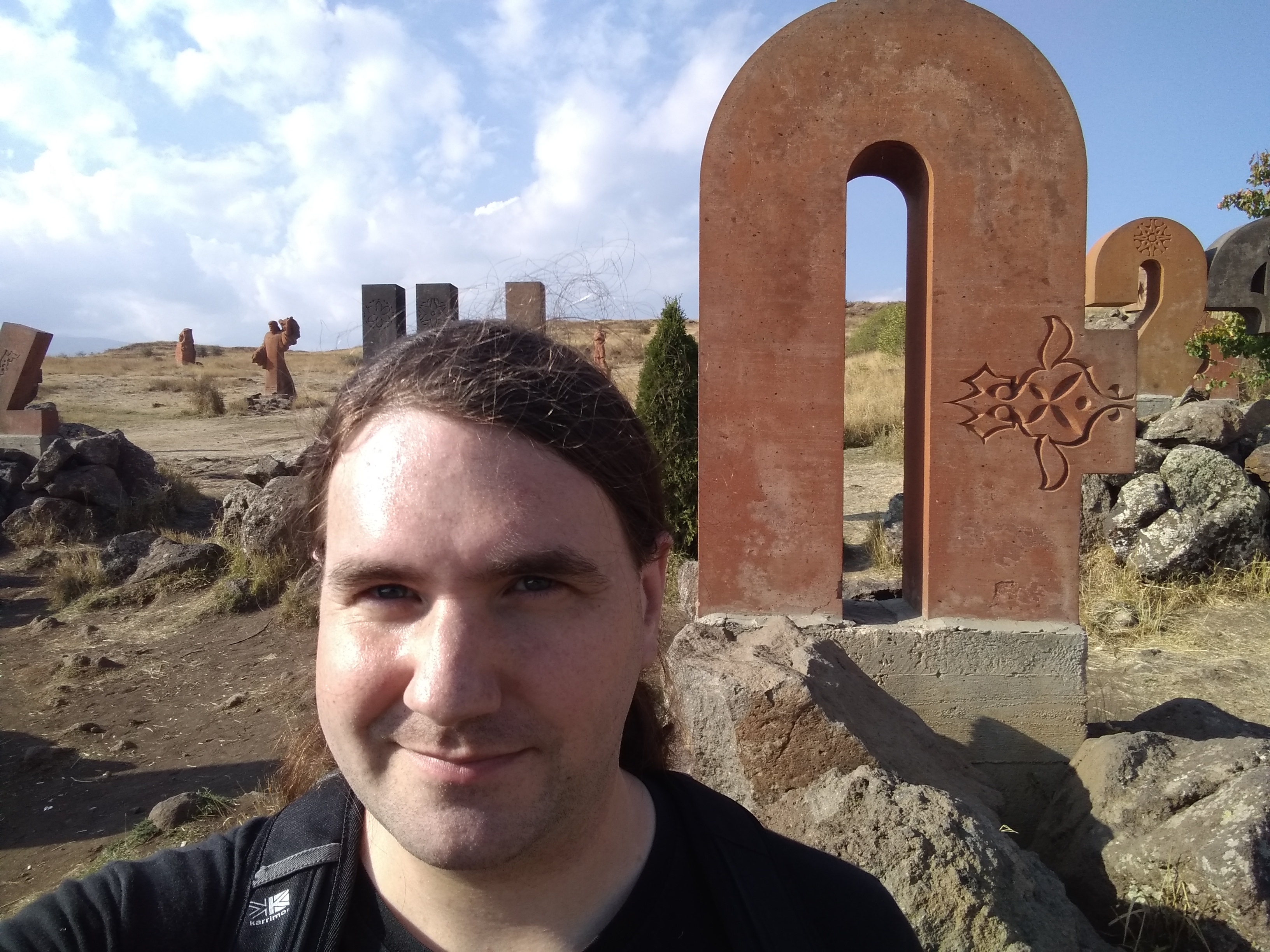 Photo of a man infront of a stone carving of an Armenian letter Ռ