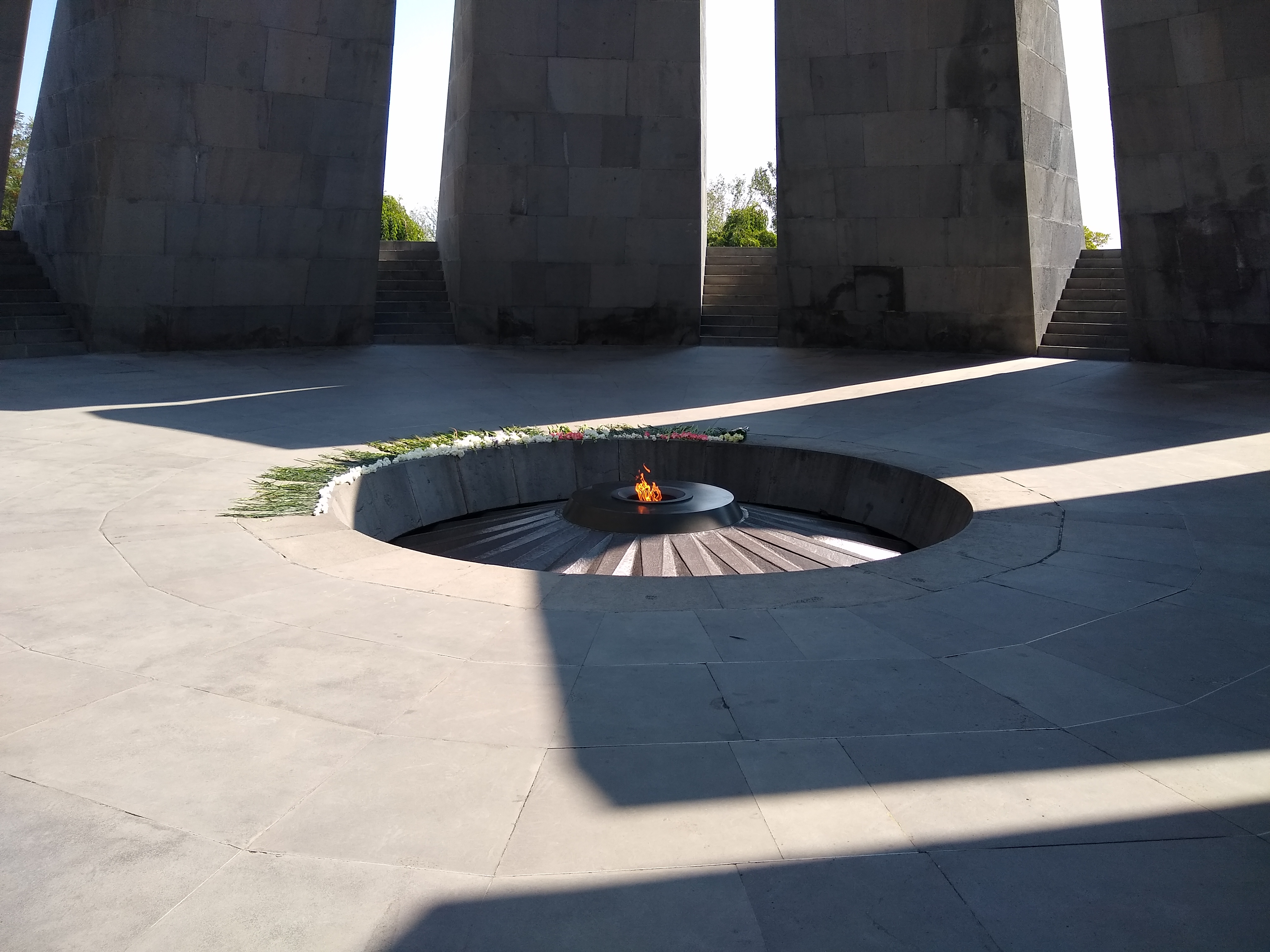 Photo of a flame inside a dome made of slabs of rock, with gaps letting light through, and staircases