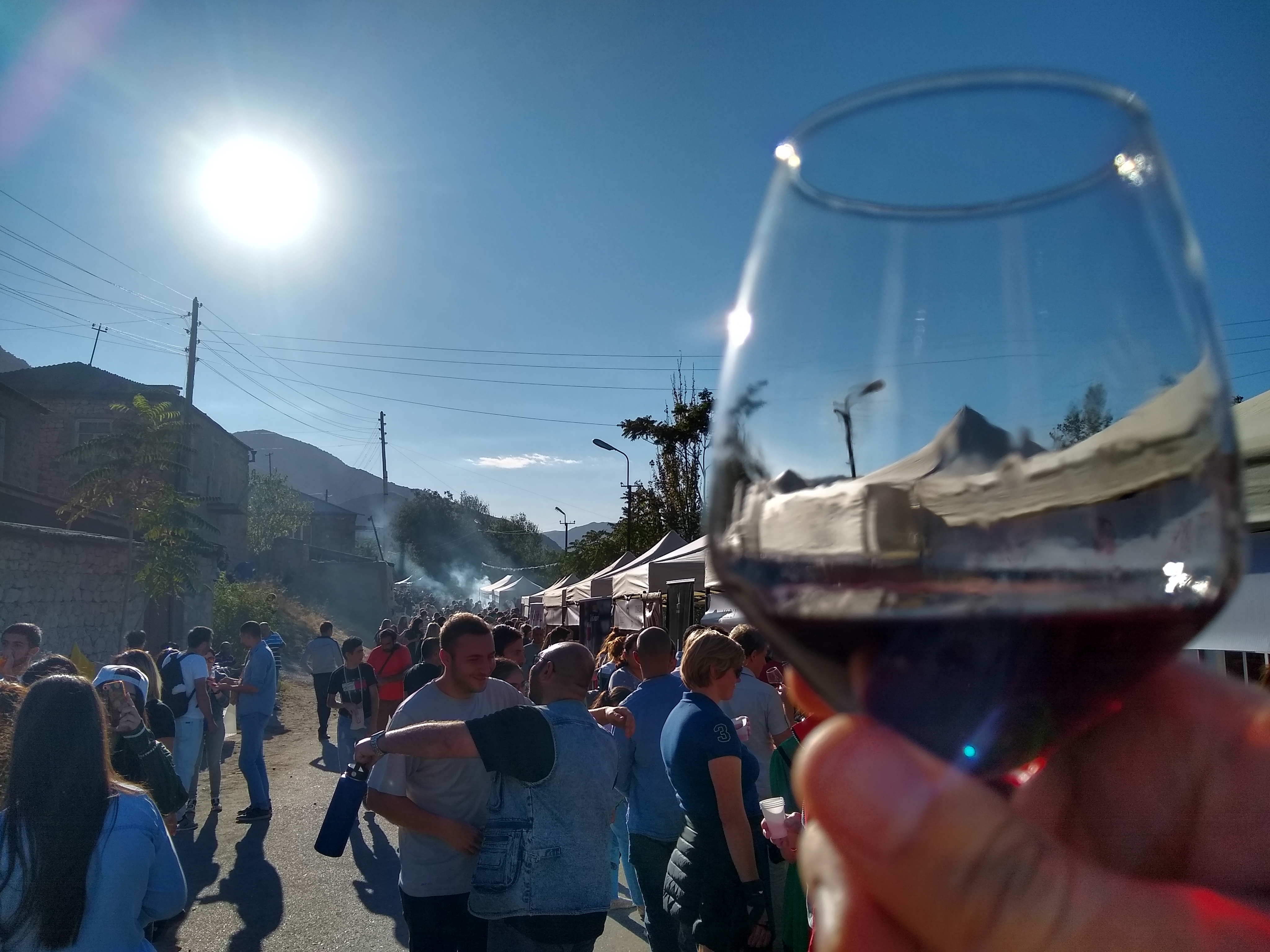 Photo of a glass of wine with people, mountains and tents in the background